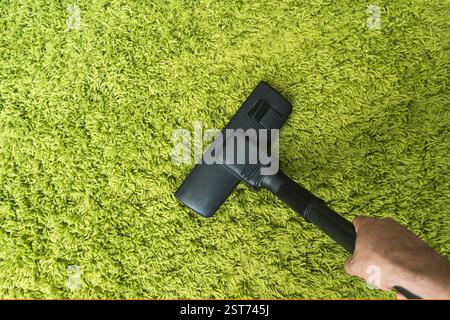 close up of hand with vacuum cleaner at home. cleaning the green carpet from dust. Home cleaning . Cleaning service. Stock Photo
