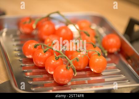 A cluster of vibrant on the vine cherry tomatoes with stems displayed on a reflective silver aluminum cooking tray, freshness and healthy eating. Stock Photo