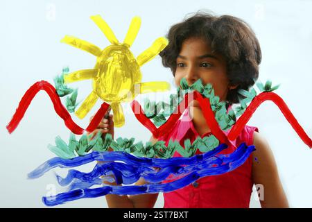 South Asian Indian eight year old girl child wearing red dress with shot hair painting with yellow, red, green, blue color on glass Stock Photo