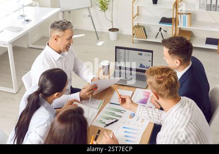 Business team sitting together at office table, doing data analysis, and using laptop Stock Photo