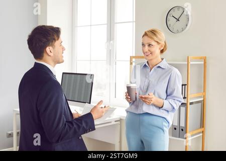 Smiling colleagues discussing work project in office, enjoying conversation during coffee break. Stock Photo