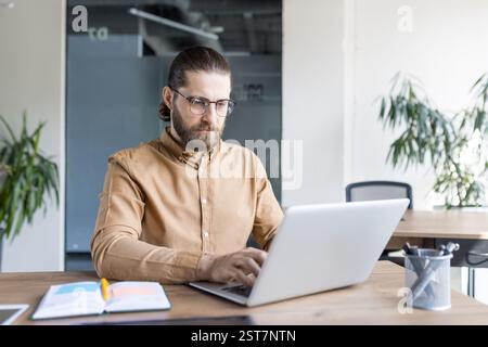 A focused office professional working on a laptop at a desk, emphasizing productivity, concentration, and modern workplace dynamics. Stock Photo