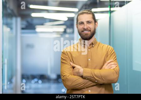 Confident individual with a friendly smile, wearing casual attire, posing in a bright office space. The image conveys professionalism, positivity, and modern workplace culture. Stock Photo
