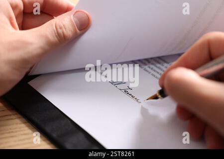 Man putting signature on document at table, closeup Stock Photo