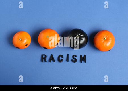 One black tangerine among orange ones and word Racism made with beads on blue background, top view Stock Photo