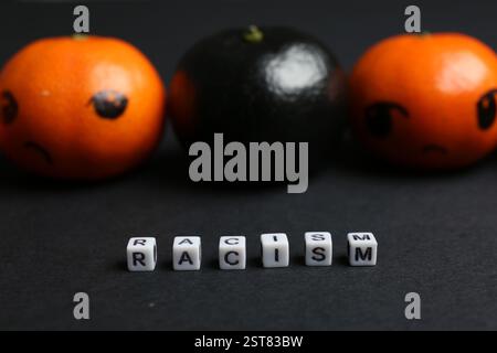 One black tangerine among orange ones and word Racism made with beads on black background, closeup Stock Photo