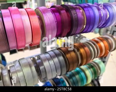 A vibrant display of various satin ribbons in different colors, neatly arranged on spools. The store is bright and inviting, perfect for craft enthusi Stock Photo