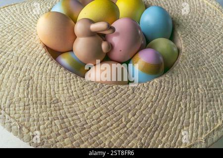 Easter concept. Pastel colored Easter eggs in straw hut as basket with ceramic bunny figure. high angle view, close up Stock Photo