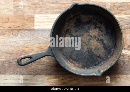 Old rusty cast iron frying pan background. On a wooden chopping cutting board. Stock Photo