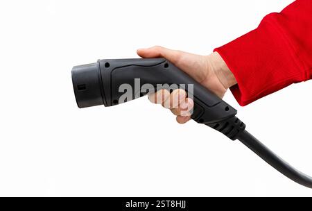 Cutout black electric vehicle charging plug in female hand wearing red sleeve. Electric car charging connector. Stock Photo