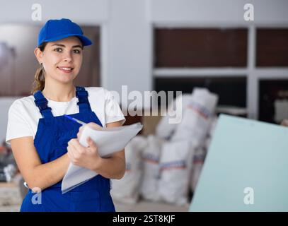 Positive young female builder contractor inspecting room and taking notes Stock Photo