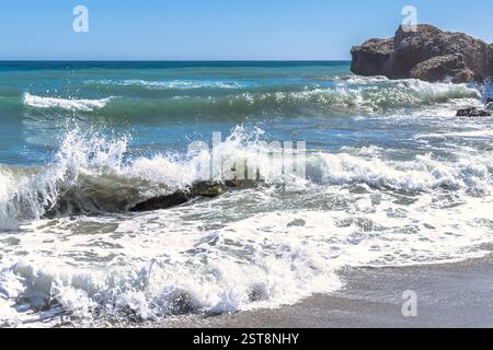 Nerja town, a resort of The Costa del Sol seaside region in Andalusia in the south of Spain. Ocean waves crashing on a rocky shore under a bright blue Stock Photo