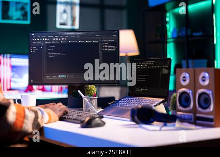 Black programmer remotely working in home office writing code on computer at his desk. Programming engineer IT expert in apartment typing lines of code at workstation, teleworking. Stock Photo