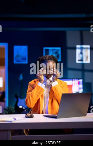 Fatigued gen Z teleworker feeling eye strain from looking too much at notebook screen while working on job tasks. Jaded freelancer removing eye glasses to relax while working from home Stock Photo