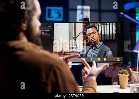 IT admin working from home in videocall with african american coworker, testing programs and systems. Programmer checking code with colleague in online teleconference, sitting at desk in apartment Stock Photo