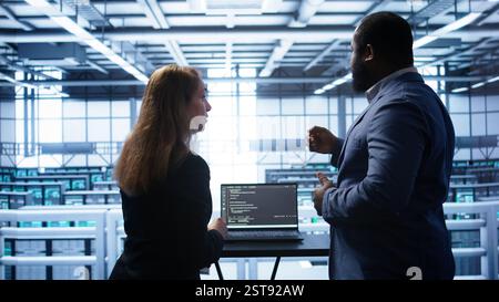 Team of engineers in data center doing brainstorming and running error checking utilities to fix problems. Teamworking colleagues in server hub looking for network issues affecting rigs, camera B Stock Photo