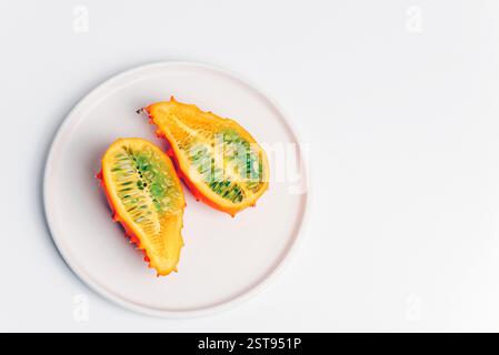 Two halves of ripe kiwano fruit with orange skin and green pulp on a white plate on white background. Stock Photo
