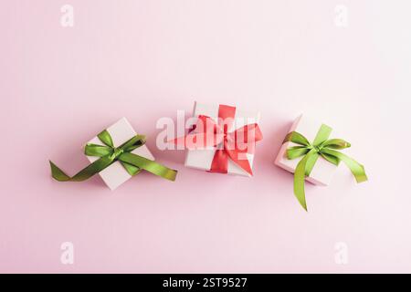 Three small gift boxes with green and red ribbons on a pastel pink background. Top view, flat lay. Stock Photo