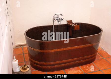 Wooden bathtub with modern shower hose inside a bathroom. Stock Photo