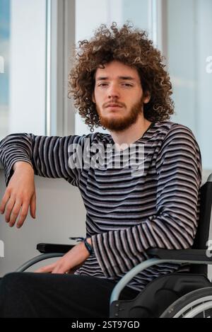 A sad young man sitting in a wheelchair by the window in the hospital. Stock Photo