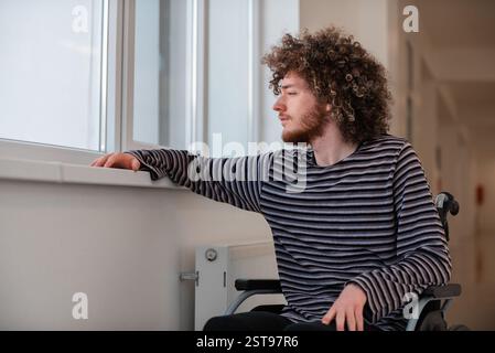A lonely sad young man sitting in a wheelchair by the window in the hospital. Stock Photo