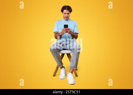 Focused guy using cellphone at studio, sitting on chair Stock Photo