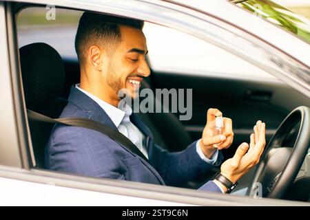 Cheerful businessman using disinfectant spray while sitting in car Stock Photo