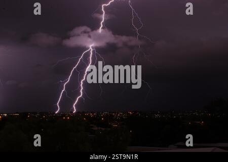 Forked lightning strike over the dark town with clear skies and one big cloud. Purple ambience. Many smaller lightning strikes. Watching lightning. Stock Photo