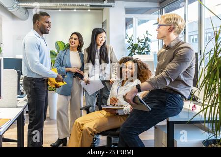 Diverse colleagues interacting, sharing ideas, and working together in a bright, open plan office space Stock Photo