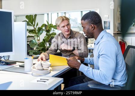 Two businessmen reviewing documents together in a modern coworking office, discussing strategies and collaborating on a project Stock Photo