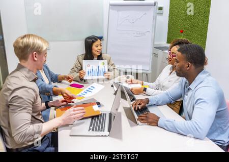 Diverse colleagues collaborating on project, analyzing graphs and charts during a productive meeting in modern coworking office Stock Photo