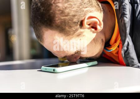 Young visually impaired man using assistive technology to interact with smartphone, touching the screen with his nose to navigate and communicate Stock Photo