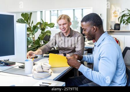 Two businessmen are working together in a coworking office, reviewing documents and collaborating on a project Stock Photo