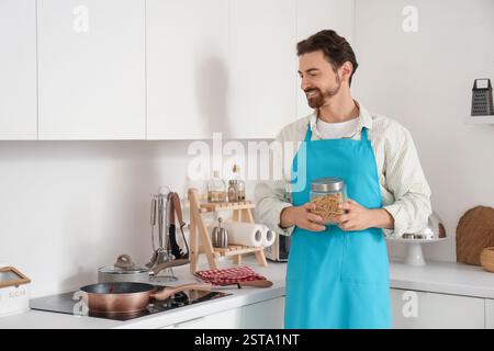 Handsome bearded man with jar of pasta and frying pan on stove in kitchen Stock Photo