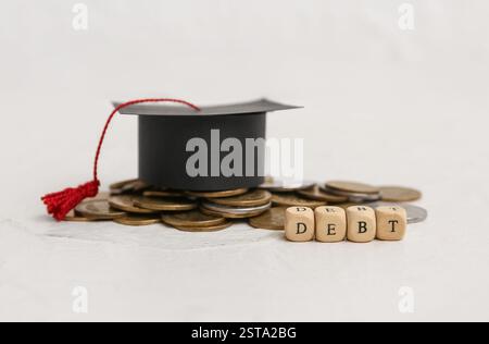 Word DEBT with graduation hat and coins on white table, closeup Stock Photo