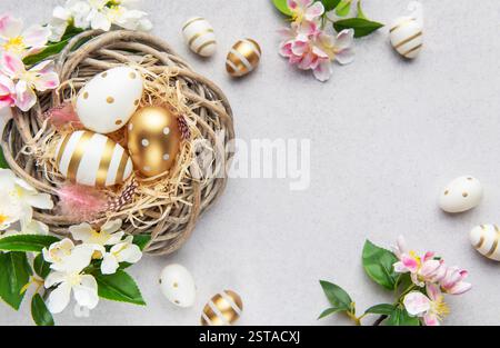 Easter eggs with gold and white decorations lying in a nest with spring flowers Stock Photo