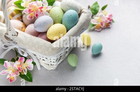 Colorful easter eggs and spring flowers overflowing from a white wicker basket on a light background Stock Photo