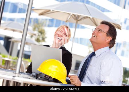 Handsome Businessman and Attractive Businesswoman Laughing While Working on the Laptop Outdoors. Stock Photo