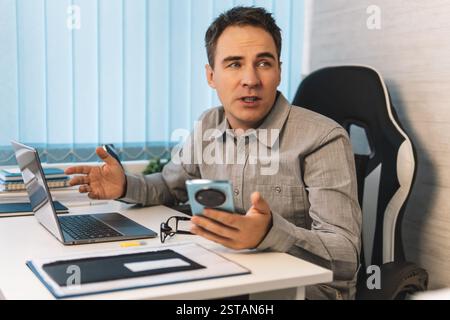 Professional Man Working on a Laptop at a Modern Office Desk During the Daytime in a Stylish Workspace. A businessman gets distracted by conversations Stock Photo