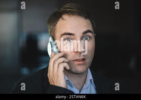photo of a perplexed young man dressed in a shirt, who is something unpleasant by phone. The call is causing confusion on the face. A businessman comm Stock Photo