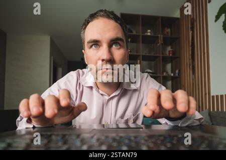 young man in eyeglasses holding laptop and looking extremely perplexed on home backdrop. Stock Photo