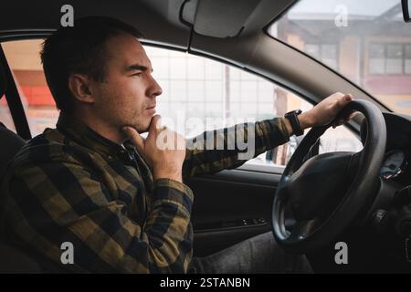 In traffic jam. dark-haired man feeling thoughtful while standing in traffic jam. The driver carefully looks out the window at the road. Stock Photo
