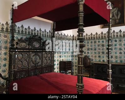 Sintra, Portugal. A magnificent bed with an elaborate canopy made of red fabric and intricate wooden posts. The walls are adorned with colorful patter Stock Photo