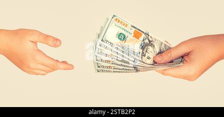Man giving dollar banknotes to woman. Female hand holding wad of hundred dollar cash bills passing it on to another person on gray background. Money Stock Photo