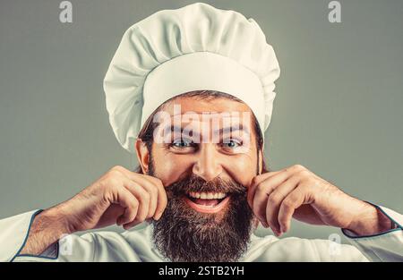 cooking, culinary and people concept - happy smiling male chef in toque. Portrait of a happy chef cook. Bearded man in chef uniform. Professional Stock Photo