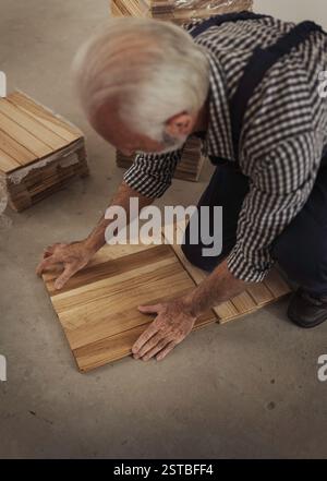 Senior craftsman installing wooden parquet on floor in apartment renovation process Stock Photo