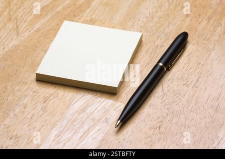 Pen and Post It Notes Pad Against a Wood Background Stock Photo
