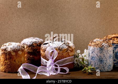 Homemade Italian traditional Easter panettone cakes in row, decorated by chocolate eggs, pink ribbon and blossoming cherry tree flowers standing on wo Stock Photo
