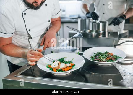 Two men is making salad. Professional chef preparing food in the kitchen. Stock Photo
