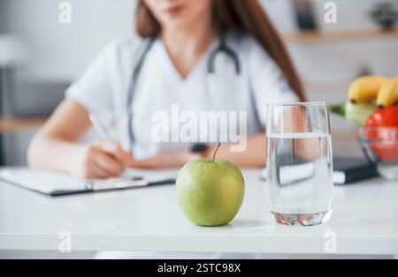 Woman writing information into the notepad. Professional medical worker in white coat is in the office. Stock Photo